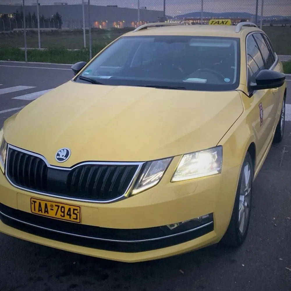Yellow Skoda estate taxi with its headlights on at dusk